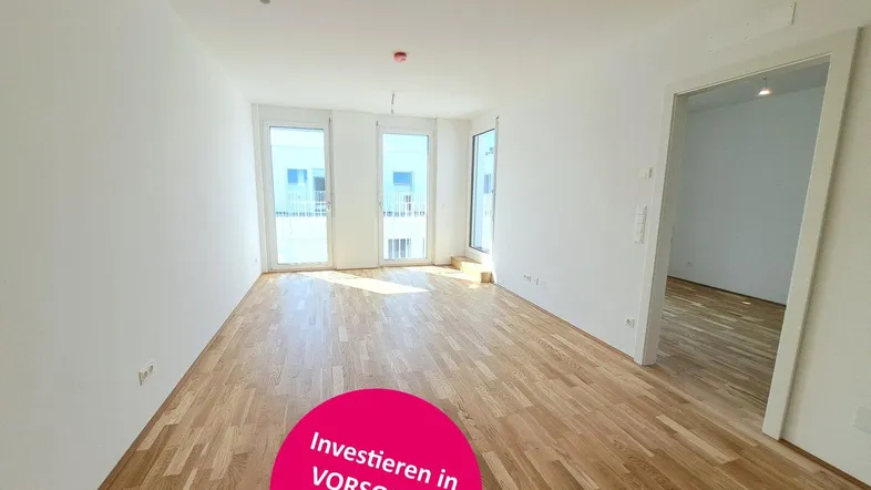 Helles Zimmer mit Parkettboden und Zugang zu einem Balkon oder einer Terrasse.
