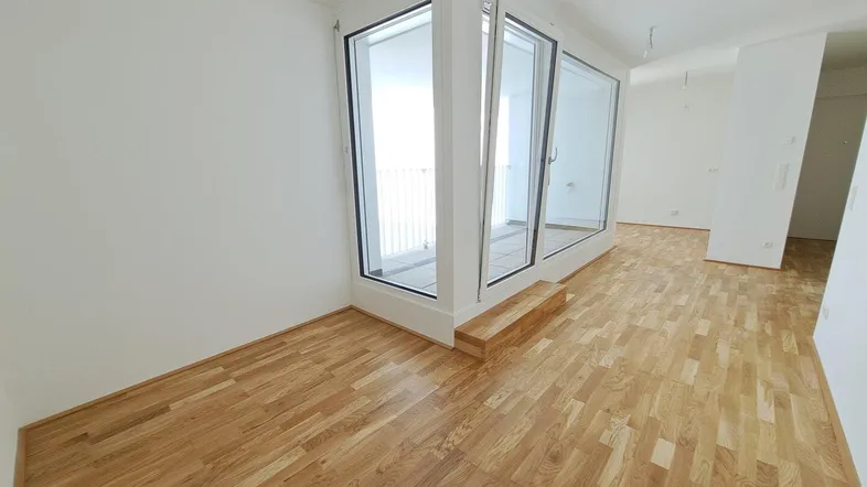 Heller Wohnbereich mit Parkettboden und großen Fenstern, die viel Tageslicht hereinlassen.