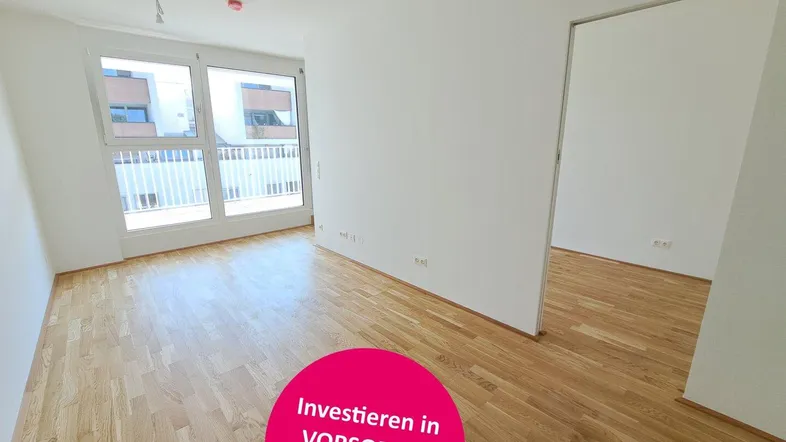 Heller, leerer Wohnraum mit Holzparkettboden und Zugang zu einem Balkon.