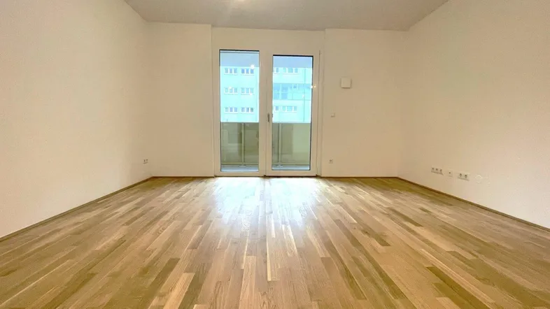 Helles, leeres Zimmer mit Parkettboden und Zugang zu einem Balkon, ideal als Wohnbereich.
