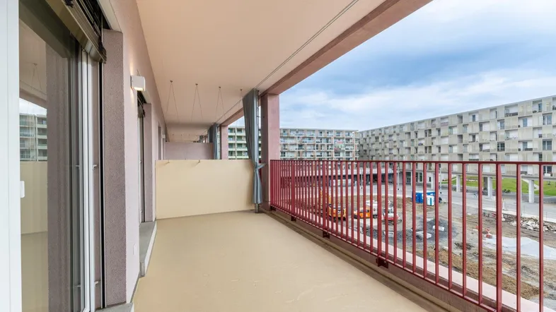 Langer Balkon mit rotem Geländer und Blick auf die umliegenden Gebäude und eine Baustelle.