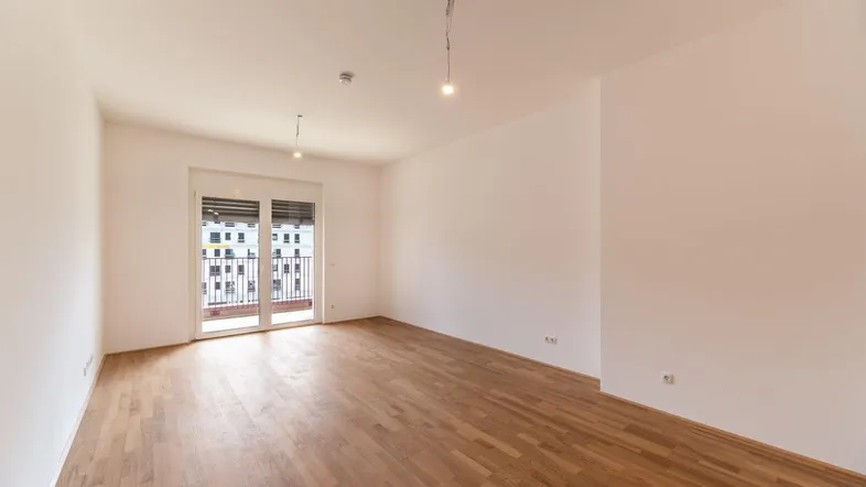 Helles, leeres Zimmer mit Holzboden und Zugang zu einem französischen Balkon.