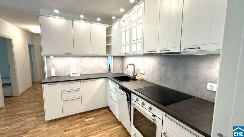 Moderne Küche mit weißen Schränken, dunkler Arbeitsplatte und Holzboden.