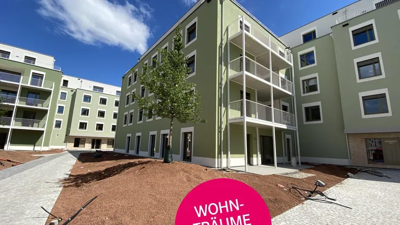 Moderne Wohngebäude mit grüner Fassade und Balkonen in einer Neubauanlage im Bau.
