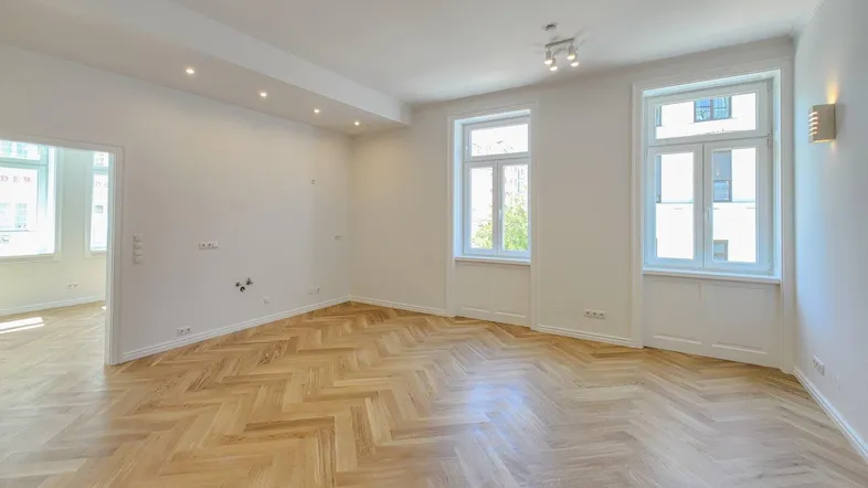 Heller, leerer Raum mit Fischgrätparkettboden und hohen Fenstern, bereit zur Einrichtung.