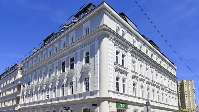 Historisches Eckgebäude mit eleganter Fassade und vielen Fenstern unter blauem Himmel.