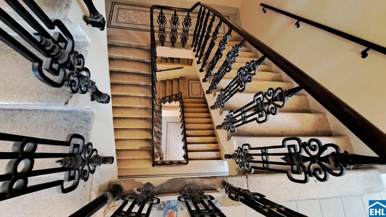 Historisches Treppenhaus mit kunstvollem schmiedeeisernem Geländer und Steinstufen in einem Altbau.