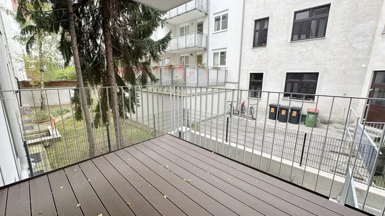 Geräumiger Balkon mit Holzboden und Blick auf den begrünten Innenhof und umliegende Gebäude.