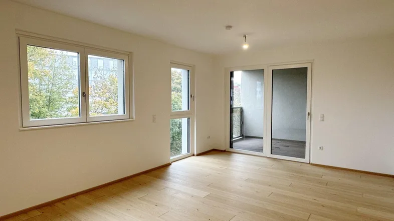 Helles, unmöbliertes Wohnzimmer mit Parkettboden und Zugang zu einem Balkon.