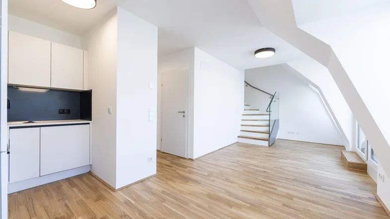 Heller, offener Wohnbereich mit integrierter Küchenzeile, Parkettboden und moderner Treppe zum Obergeschoss.