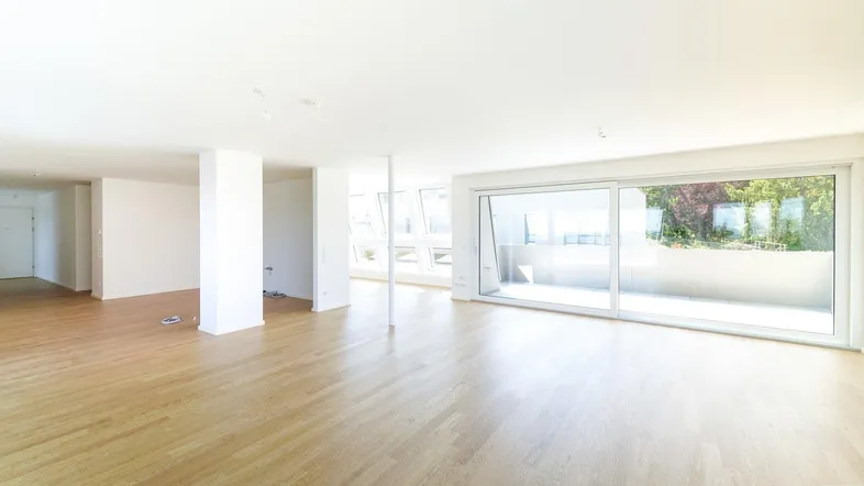 Helles, offenes Wohnzimmer mit Holzboden und großen Schiebetüren, die zu einer Terrasse führen.