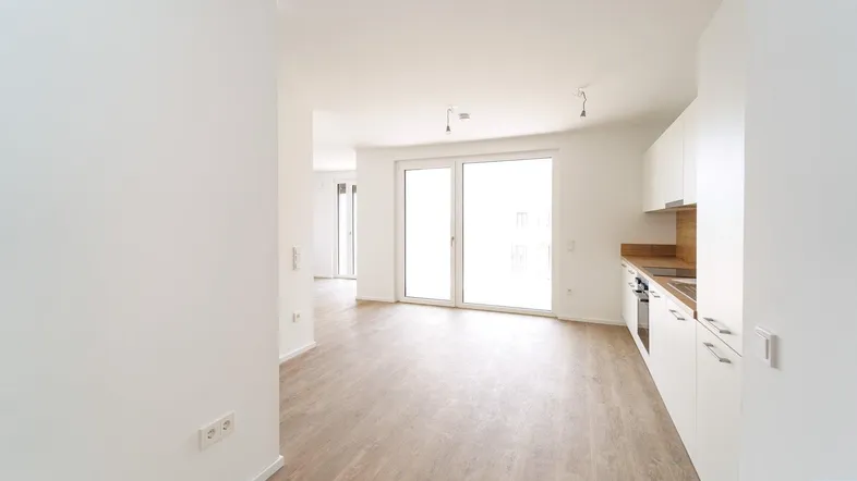Offener Wohnbereich mit integrierter Küche, hellem Laminatboden und großem Fenster zum Außenbereich.