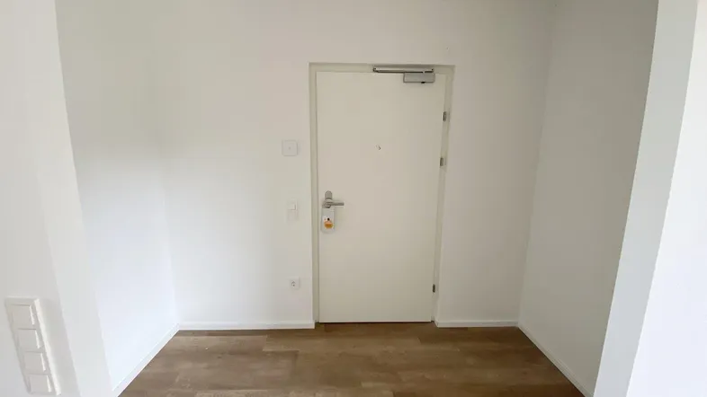 Heller Eingangsbereich mit Laminatboden und weiß gestrichenen Wänden, der zu den Wohnräumen führt.