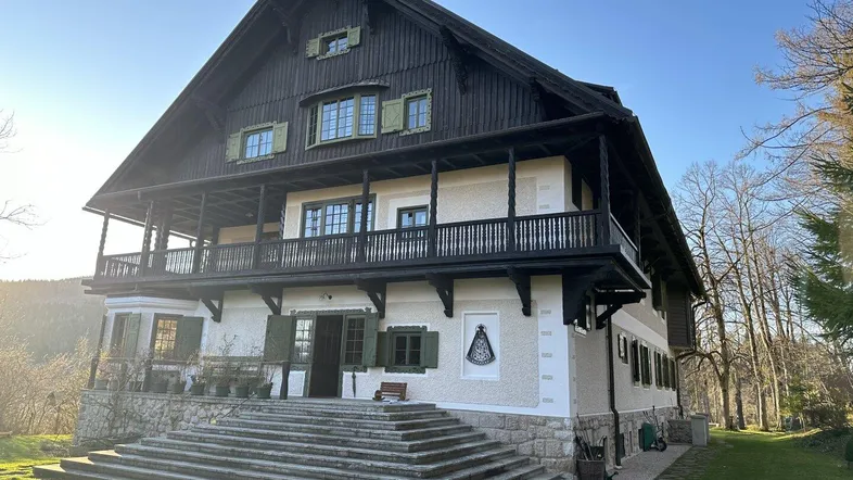 Großes, traditionelles Haus mit Holzfassade und mehreren Balkonen in ländlicher Umgebung.