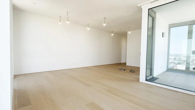 Heller, unmöblierter Wohnbereich mit Holzboden und großen Fenstern, die viel Tageslicht hereinlassen.