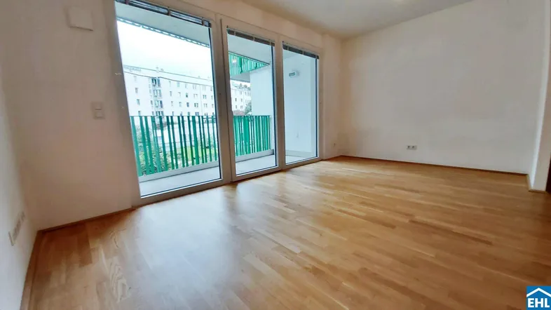 Helles Wohnzimmer mit Parkettboden und Zugang zu einem Balkon mit grüner Brüstung.