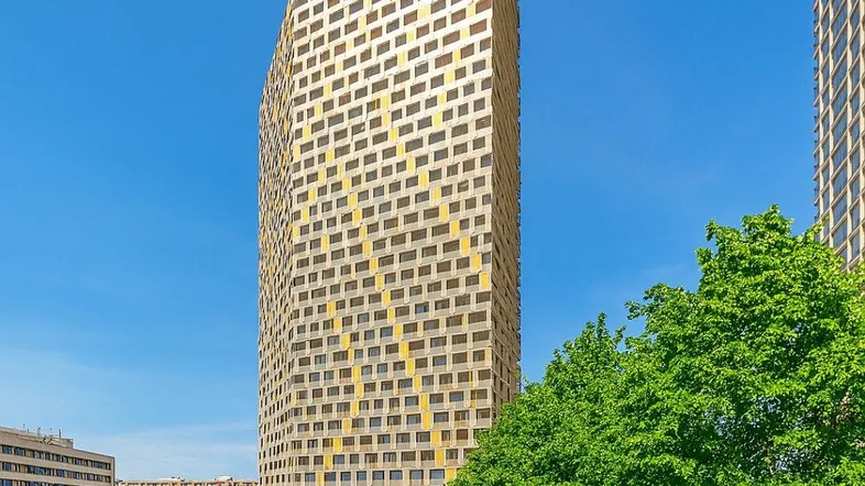 Modernes Hochhaus mit markanter Fassade und vielen Fenstern unter blauem Himmel.