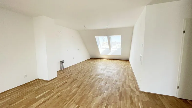 Helles, leeres Zimmer mit Dachschrägen, Parkettboden und Dachfenstern, bereit für die Einrichtung.