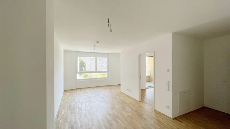 Helles, leeres Wohnzimmer mit Parkettboden und großen Fenstern, bereit zur individuellen Gestaltung.