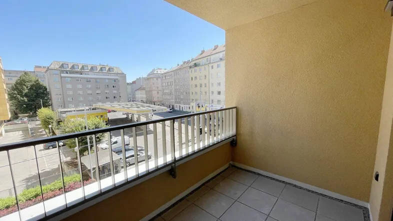 Geräumiger Balkon mit Fliesenboden und Blick auf die umliegenden Stadtgebäude unter blauem Himmel.