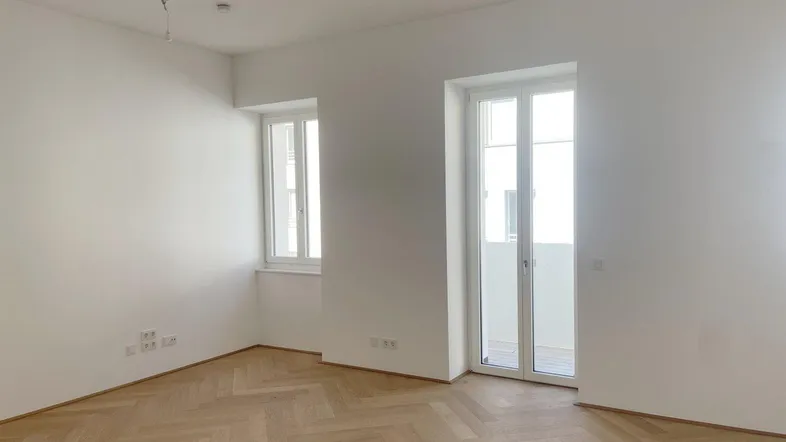 Heller Raum mit Fischgrätparkettboden und Zugang zu einem französischen Balkon.