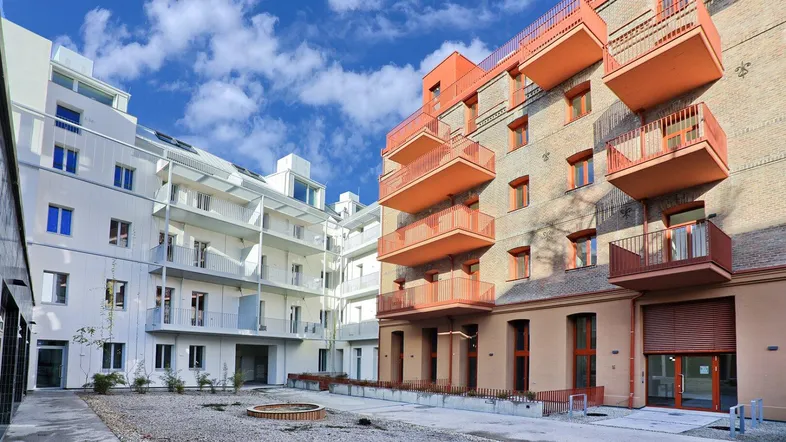 Moderne Wohnanlage mit zwei Gebäuden, farbigen Balkonen und einem begrünten Innenhof.