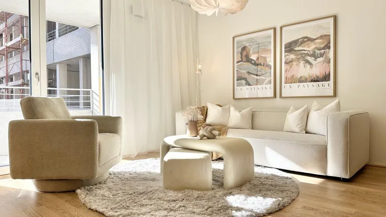 Helles Wohnzimmer mit modernem Sofa, Sessel und Zugang zu einem Balkon.