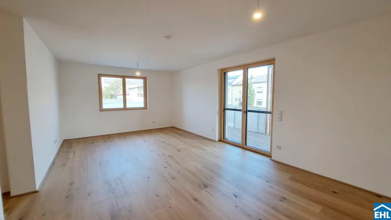 Helles, leeres Zimmer mit Holzboden und Zugang zu einem Balkon, ideal für einen Wohnbereich.