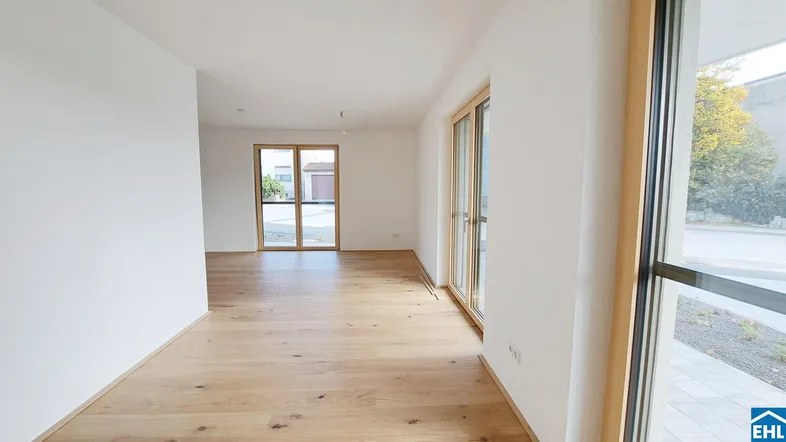 Heller, leerer Raum mit Holzboden und großen Fenstertüren, die viel Tageslicht hereinlassen.
