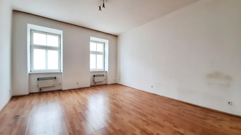 Helles, leeres Zimmer mit Parkettboden und zwei Fenstern, ideal als Wohn- oder Schlafzimmer.