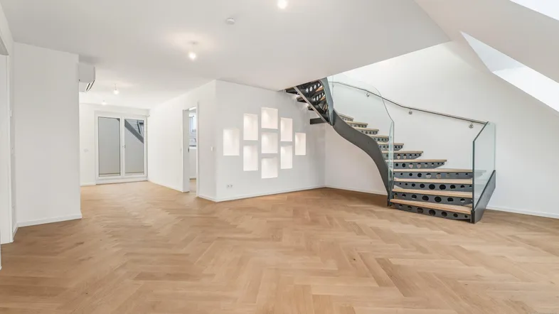 Geräumiger Wohnbereich mit modernem Fischgrätparkett und eleganter Wendeltreppe mit Glasgeländer.