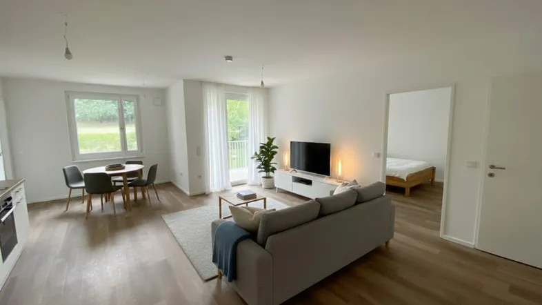 Heller, offener Wohn- und Essbereich mit Holzboden, modernen Möbeln und Zugang zum Balkon.