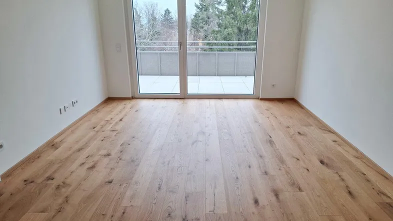 Heller Wohnraum mit neuem Parkettboden und Zugang zu einer großen Terrasse.