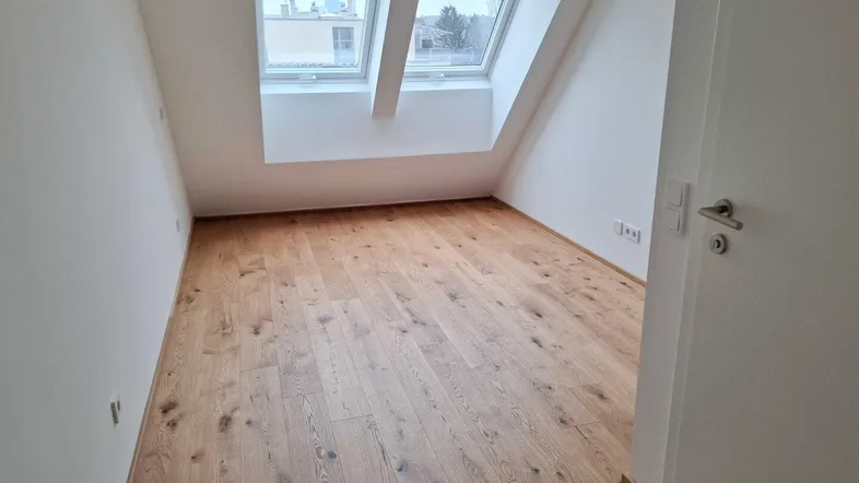 Heller Raum im Dachgeschoss mit schrägen Wänden, Holzboden und Dachfenstern.