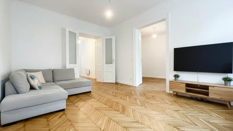 Geräumiges Wohnzimmer mit hellem Fischgrätparkett, modernem Sofa und Fernseher.