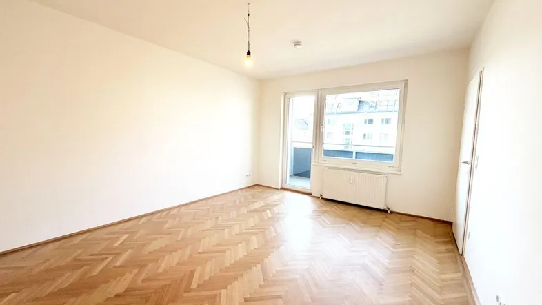 Helles Wohnzimmer mit Fischgrätparkett, weißen Wänden und Zugang zu einem kleinen Balkon.
