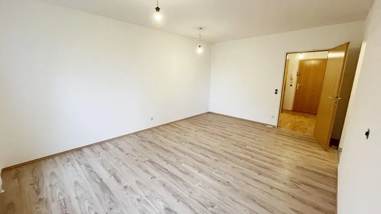 Helles, leeres Zimmer mit Laminatboden und weiß gestrichenen Wänden, bereit zur individuellen Gestaltung.
