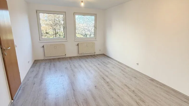 Helles Zimmer mit neuem Laminatboden und zwei Fenstern, ideal als Wohn- oder Schlafbereich.