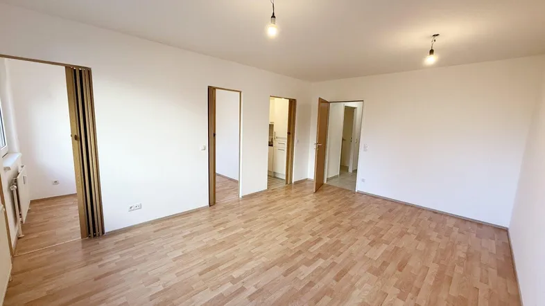 Geräumiges Wohnzimmer mit hellem Laminatboden und mehreren Türen zu angrenzenden Räumen.