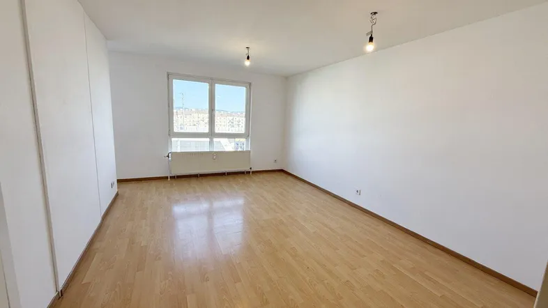 Helles, leeres Zimmer mit Holzfußboden und großem Fenster, bereit zur individuellen Gestaltung.