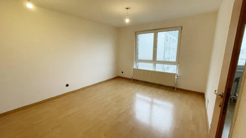 Helles, leeres Zimmer mit Parkettboden und großem Fenster, bereit zur individuellen Gestaltung.