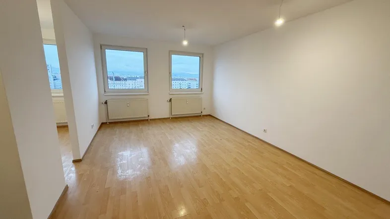 Helles, leeres Zimmer mit Laminatboden und zwei Fenstern, ideal als Wohn- oder Schlafbereich.
