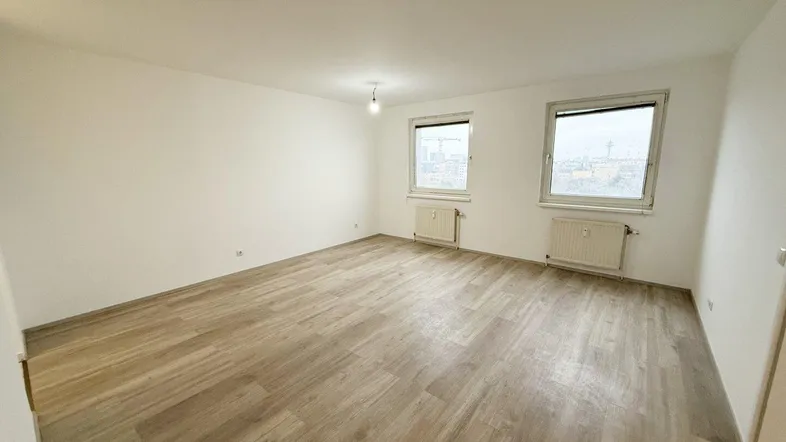 Helles, leeres Wohnzimmer mit modernem Laminatboden und zwei Fenstern, bereit zum Einzug.