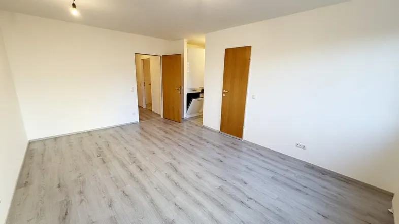 Helles, leeres Zimmer mit modernem Laminatboden und mehreren Türen, bereit zur individuellen Gestaltung.