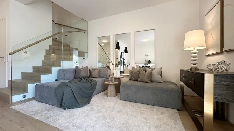 Helles Wohnzimmer mit modernem Sofa, Teppich und offener Treppe mit Glasgeländer.