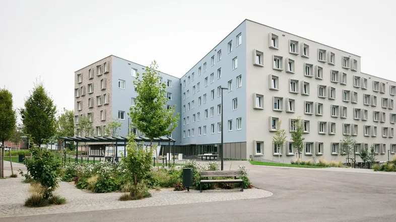 Moderne Wohnanlage mit mehreren Gebäudeflügeln, umgeben von Grünflächen und einem gepflasterten Vorplatz.