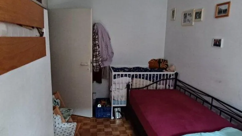 Helles Schlafzimmer mit Parkettboden, einem Bett und einem Kinderbettchen.