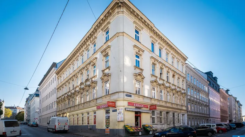 Historisches Eckgebäude mit klassischer Architektur und Geschäften im Erdgeschoss an einer Stadtstraße.