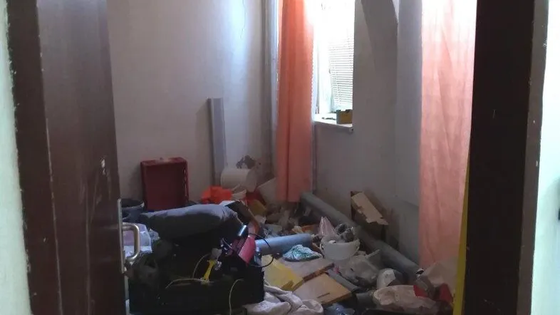 Ein unaufgeräumter Innenraum in einem renovierungsbedürftigen Zustand mit einem Fenster und Holzdecke.