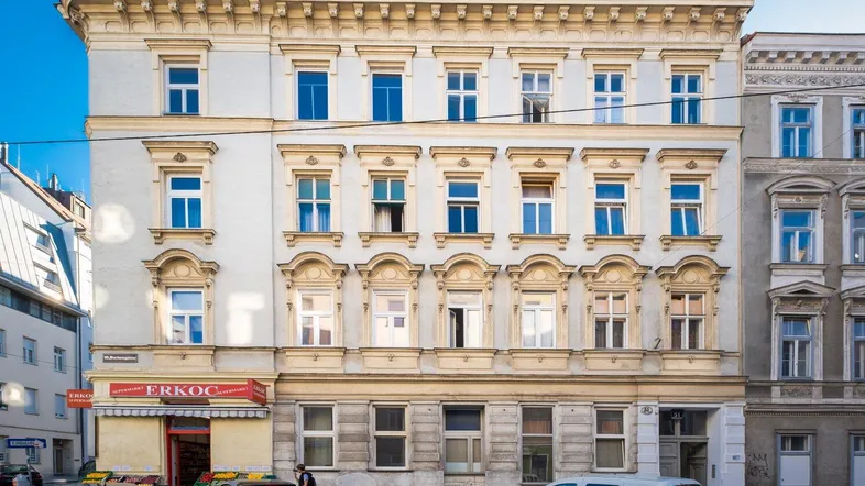 Historisches Mehrfamilienhaus mit klassischer Fassade und Geschäften im Erdgeschoss an einer belebten Straße.